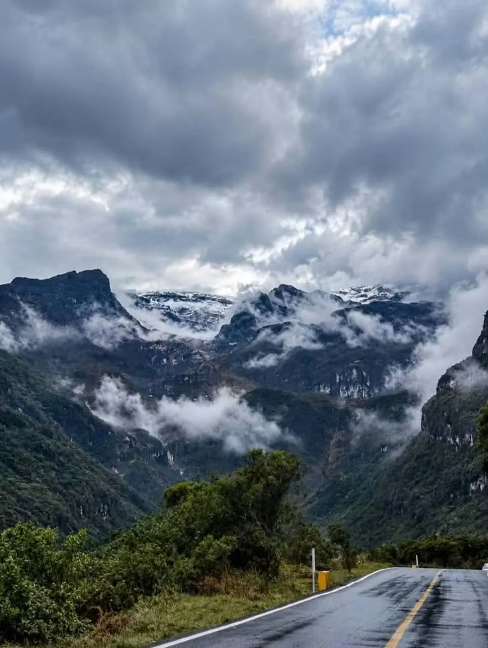 Montañas nevadas entre nubes sobre una vía mojada
